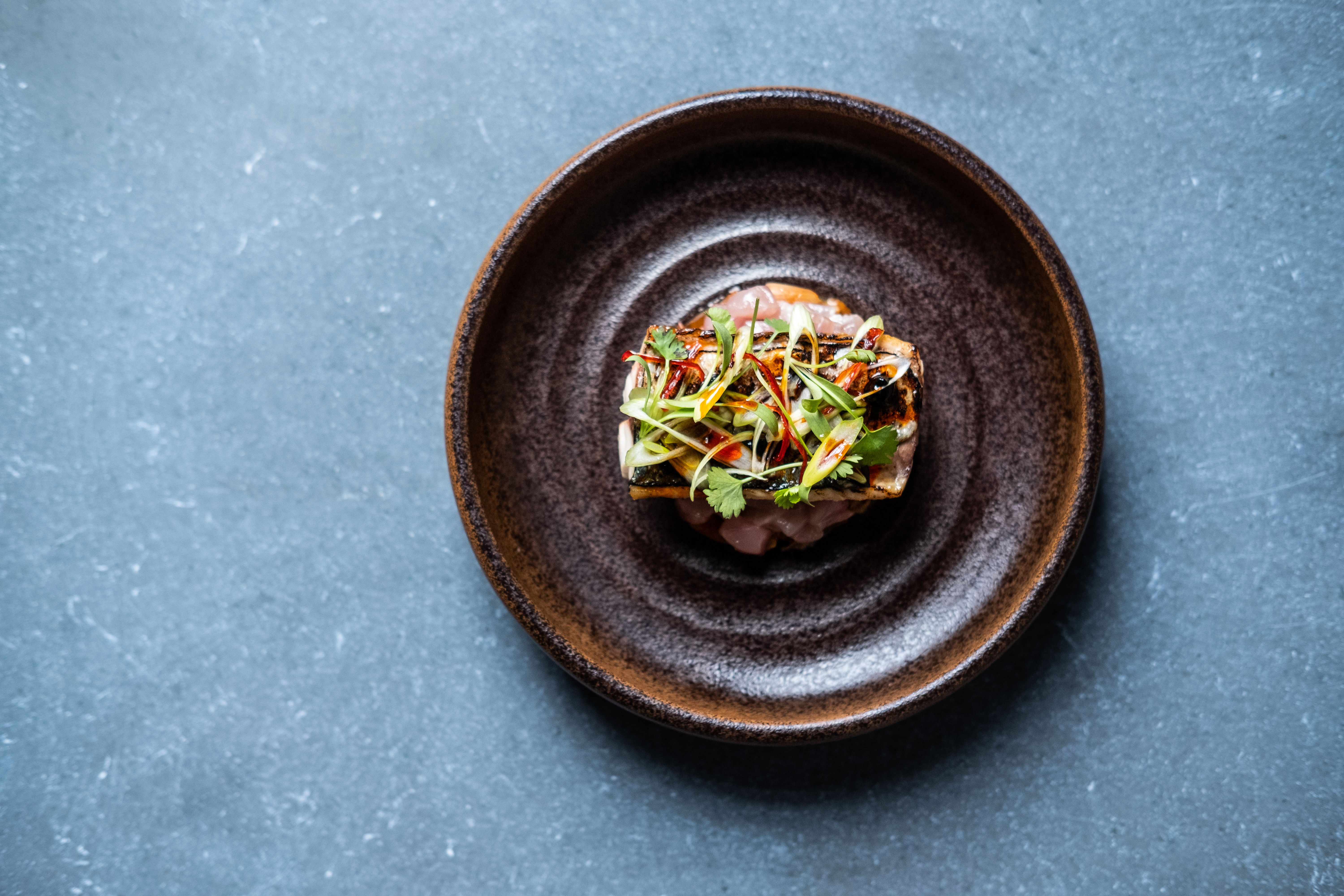 A dish garnished with herbs and vegetables on a brown plate.