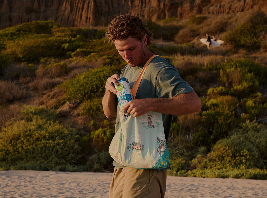 A person checking a bag on a beach at sunset.