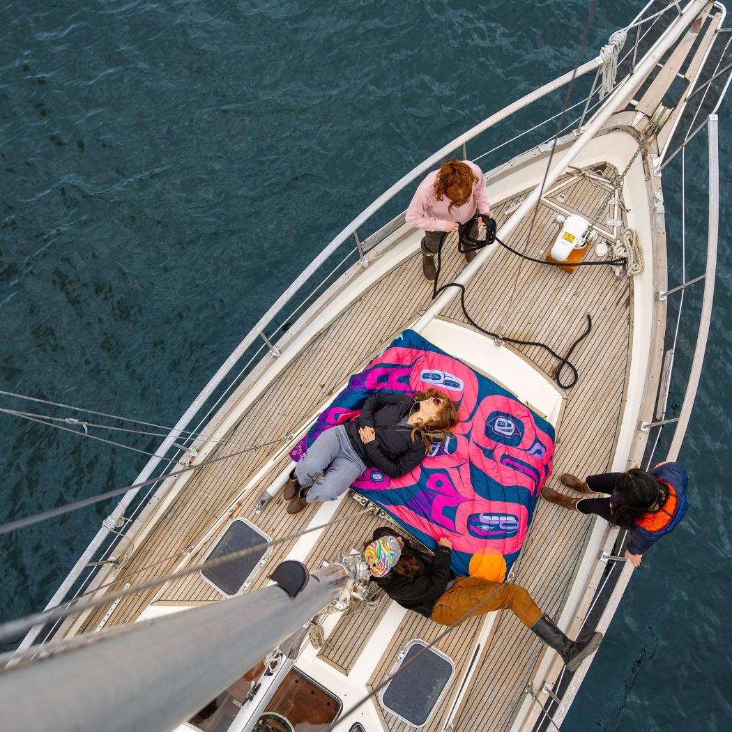 Four people relaxing on a sailboat with colorful blankets.
