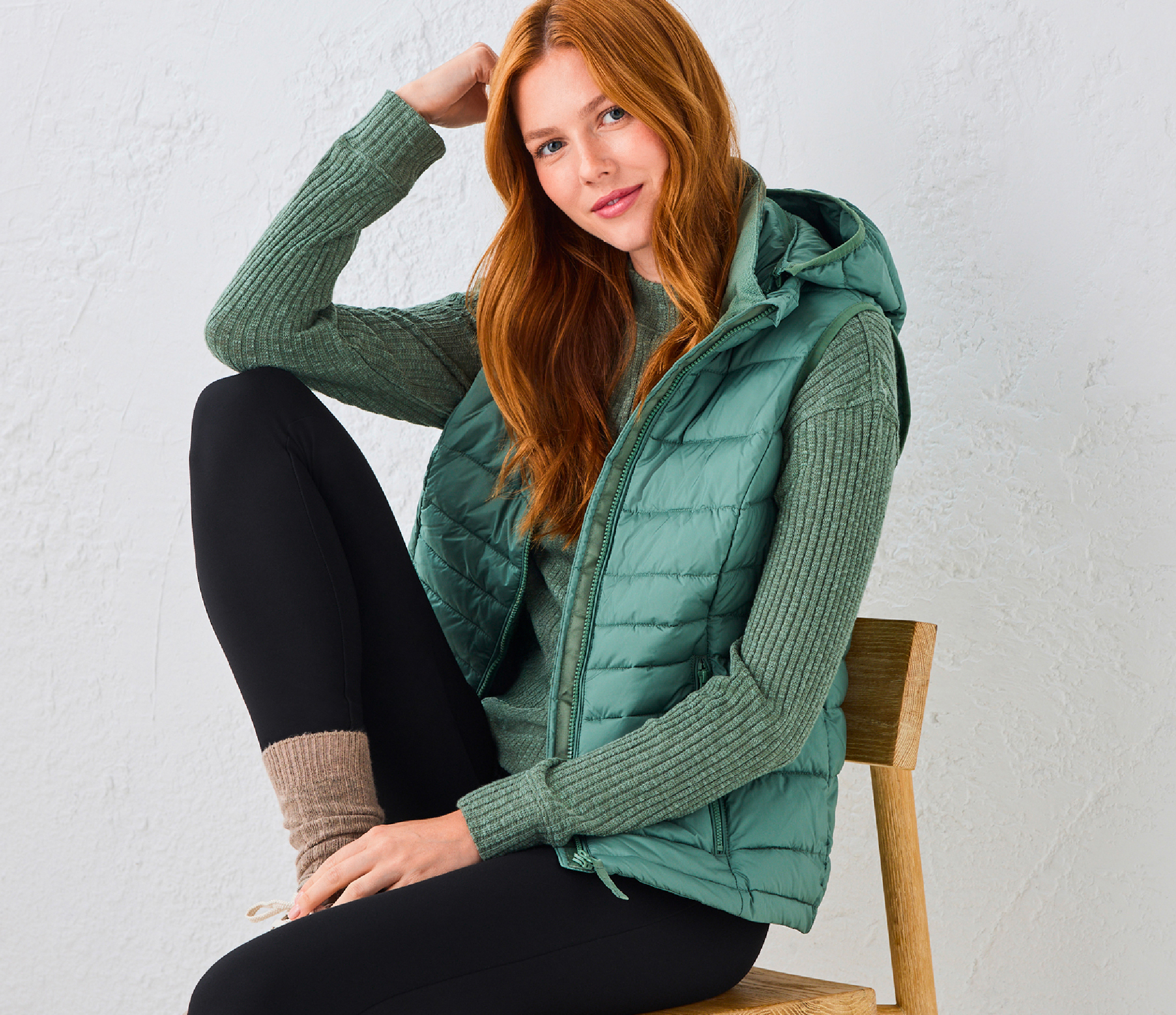 Woman in a green vest sitting on a chair, wearing leggings and smiling.