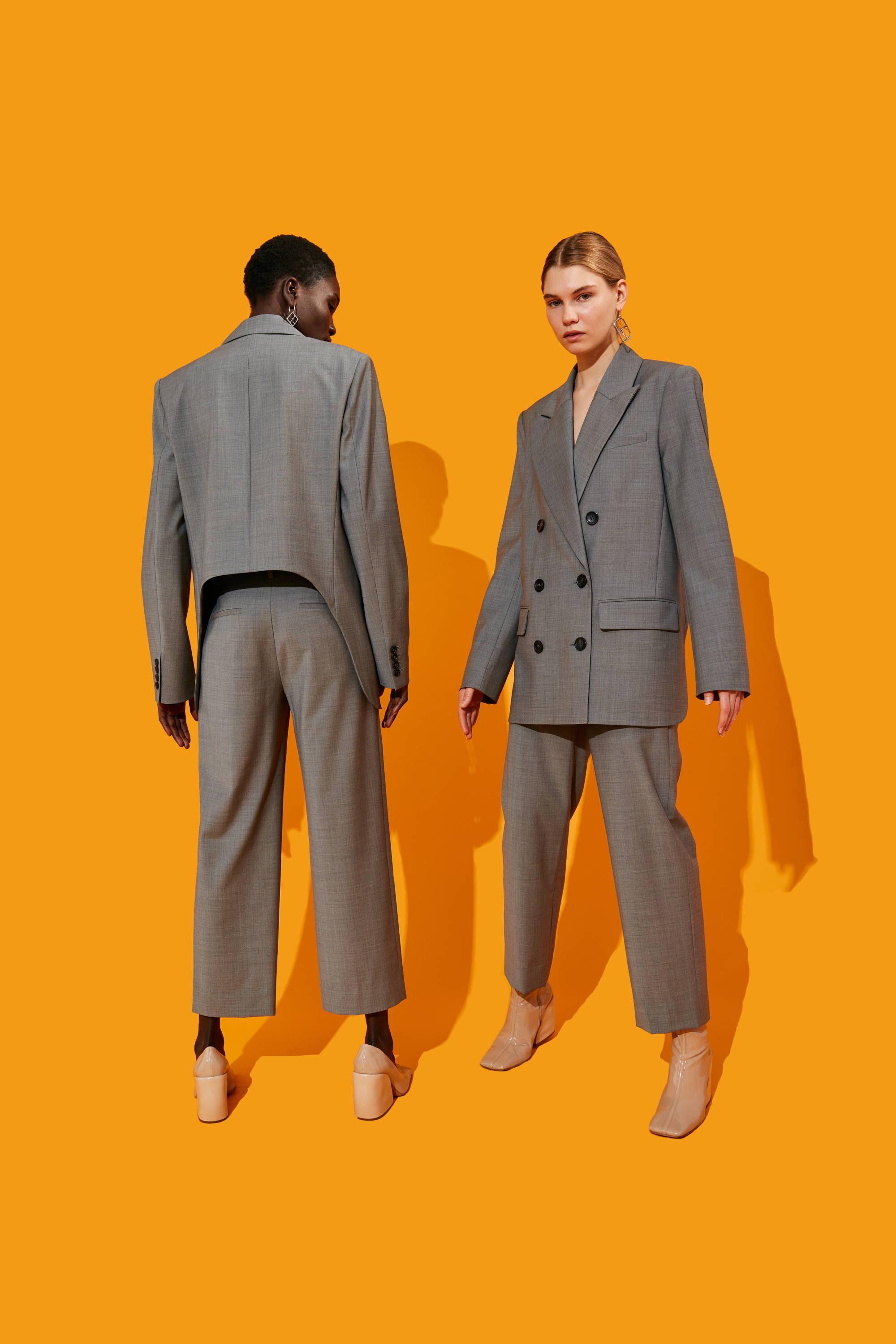 Two models wearing gray suits against an orange background.