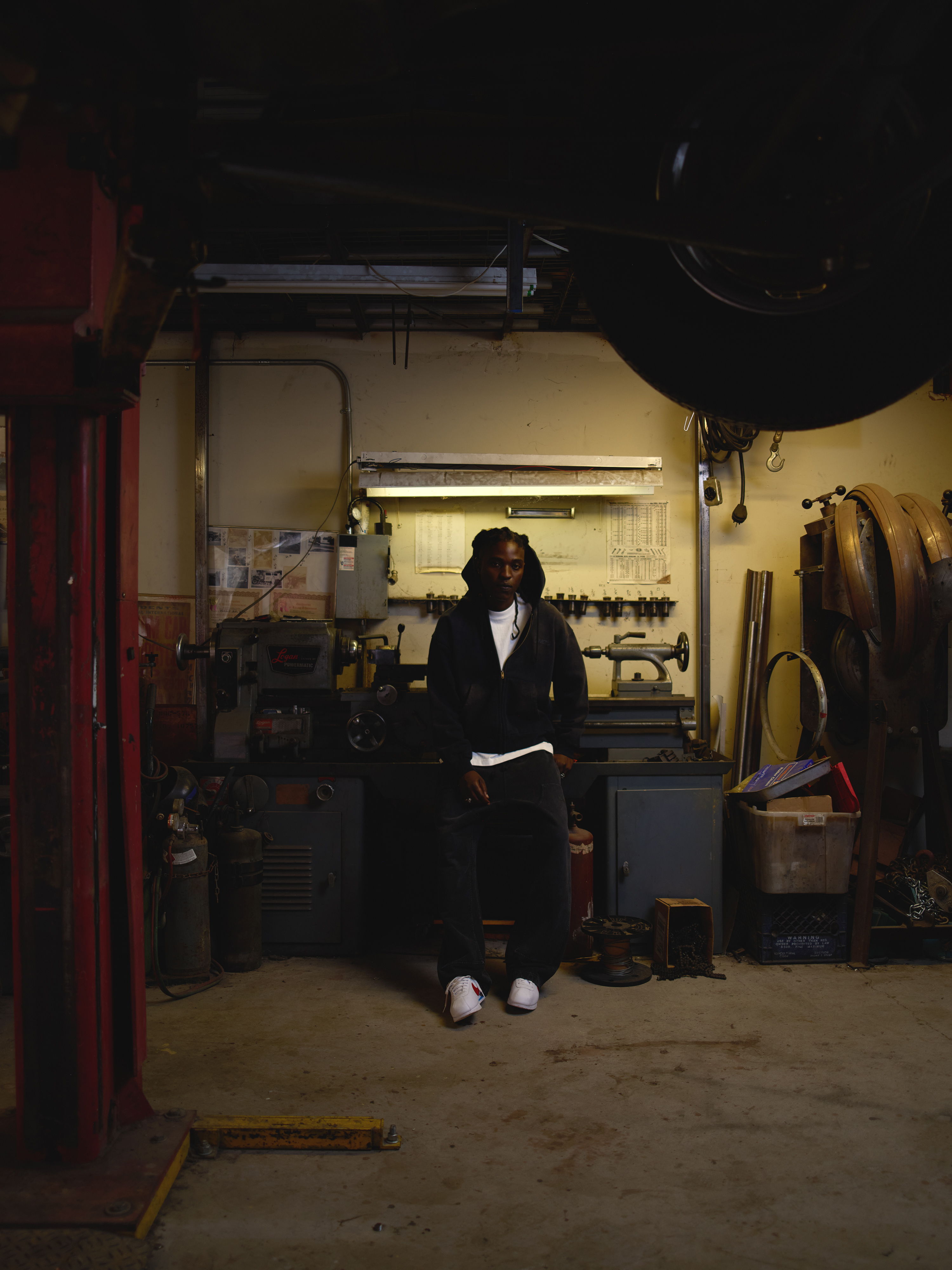 Person sitting in a garage surrounded by tools and equipment.