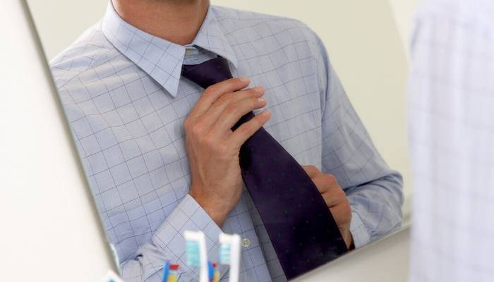 Man tying necktie in mirror