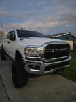 Low-angle front-three-quarter view of white lifted RAM 2500 Heavy Duty with black wheels parked in suburban driveway