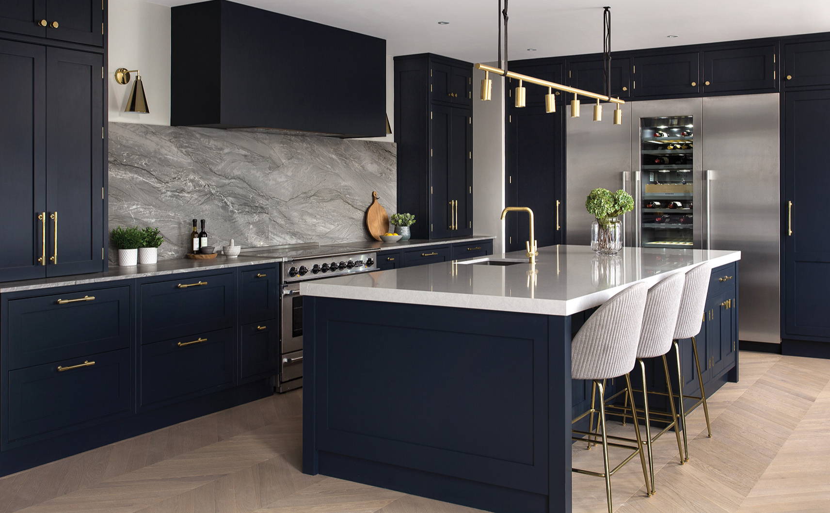 Navy kitchen with brass handles, stainless steel appliances, marble worktops and wooden flooring