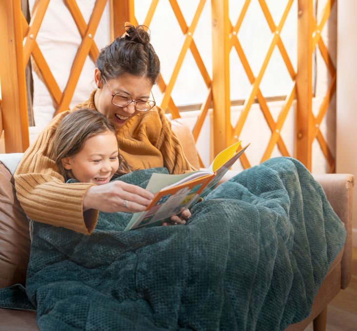 A woman and child reading together under a cozy blanket.