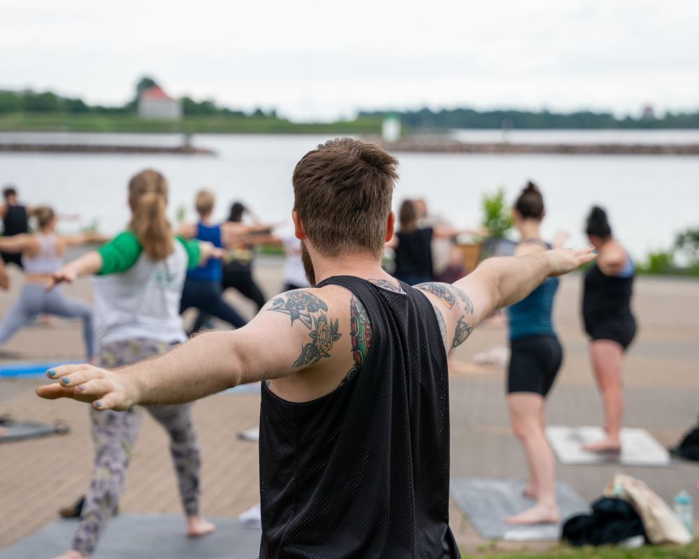 Group yoga class by the water, participants in various poses.