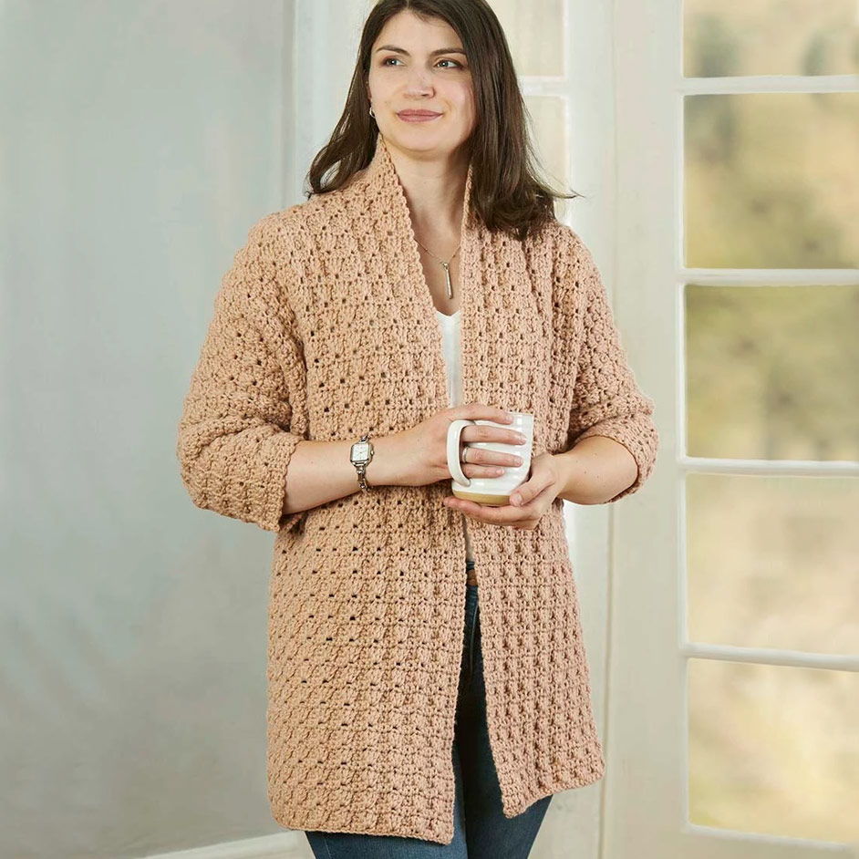 Woman in a cozy crocheted cardigan holding a mug.
