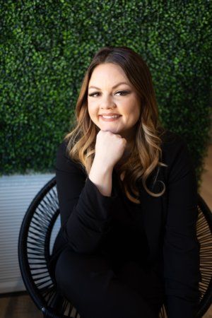 Smiling woman sitting in a chair with green foliage background.