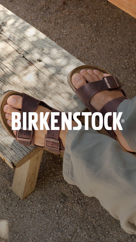A person's feet wearing brown Birkenstock sandals on a wooden bench.