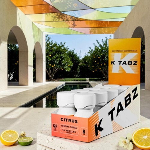 Box of K TABZ citrus drink near a pool surrounded by greenery.