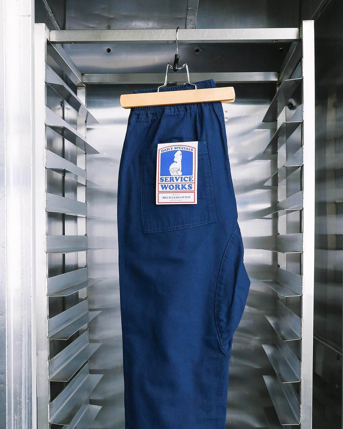 A look book image of a pair of Service Works Canvas Chef Trousers hung up in a kitchen.