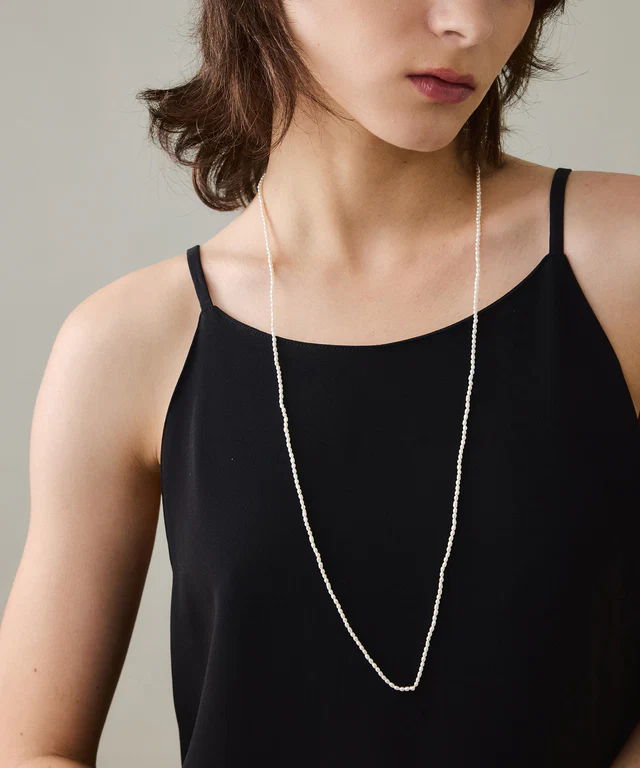 A close-up of a woman wearing a black top and a long necklace.