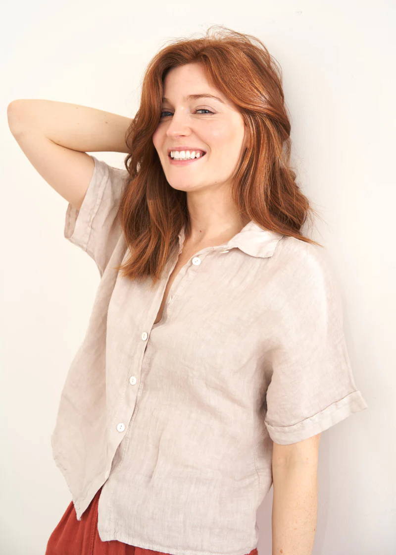 A model wearing a light pink cropped linen shirt with mother of pearl buttons 