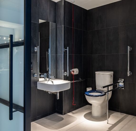 Modern accessible bathroom with black tiles, toilet, and sink.