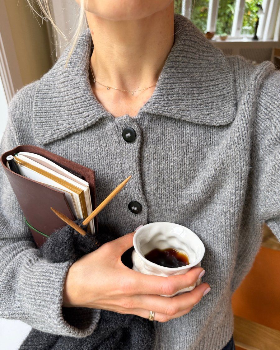 Kvinde iført Petra Jacket med kafe og notesbog i hænderne
