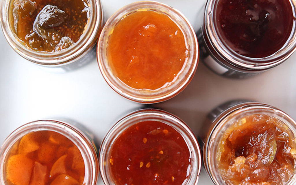 Six jars of jam are open and reveal the different colors of jam inside the jars. 
