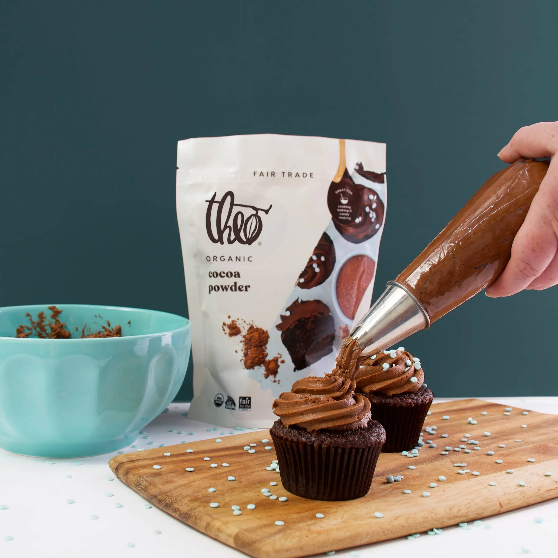 Cupcakes being frosted with baking bowl and Cocoa Powder in background