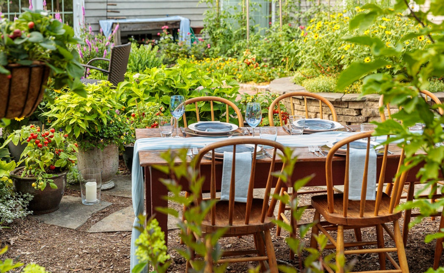 Dinner table and chair set up in the backyard surrounded by veggie garden