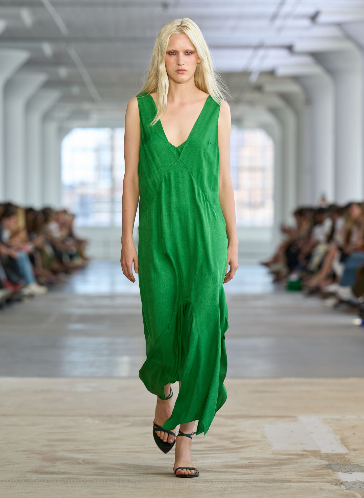 Model in a green dress walking down a runway with an audience.