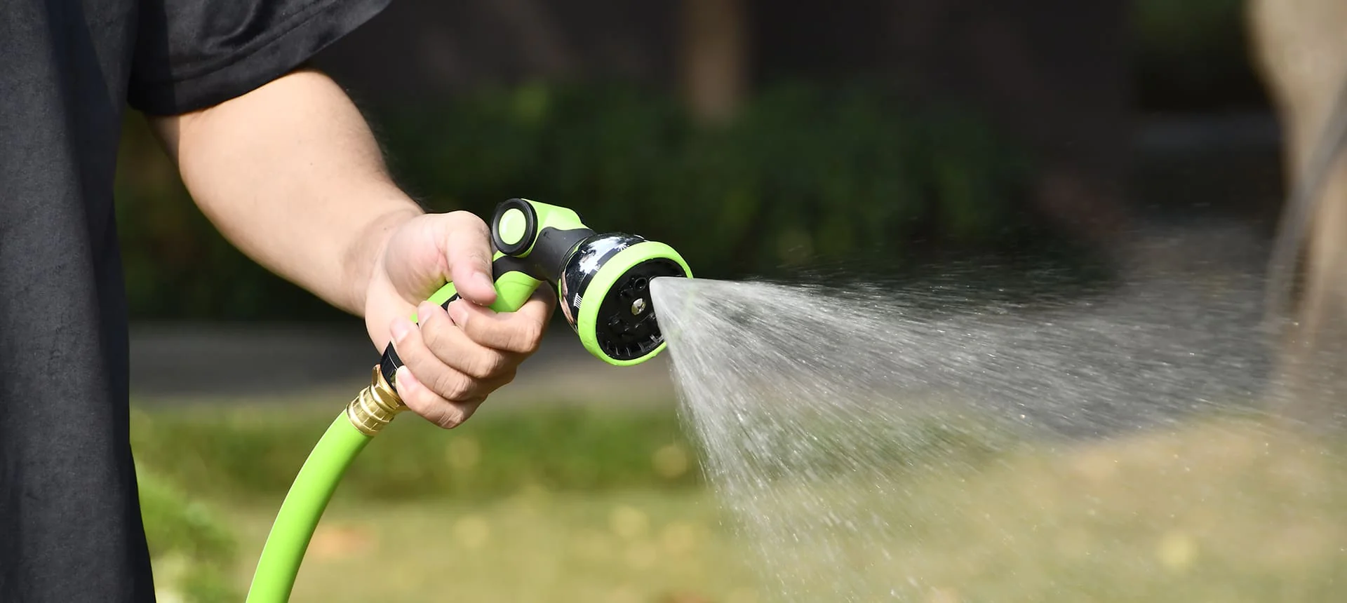 A person watering plants with a green garden hose.