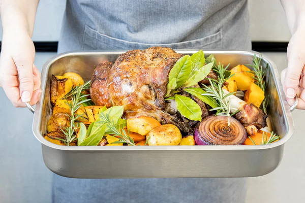 A roast leg of lamb in a roasting tin with vegetables