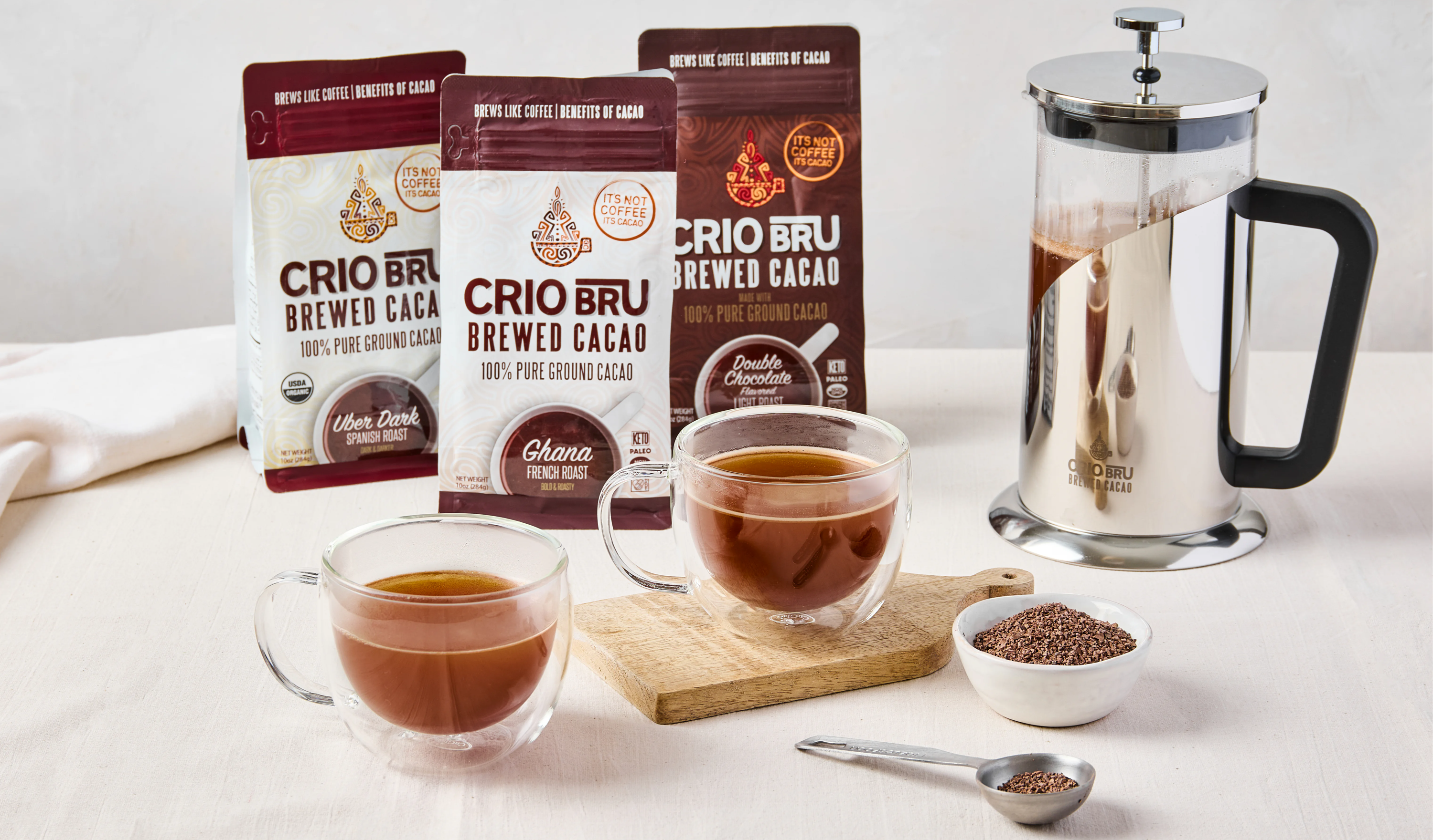 Coffee products, two cups of brewed coffee, and a French press on a table.