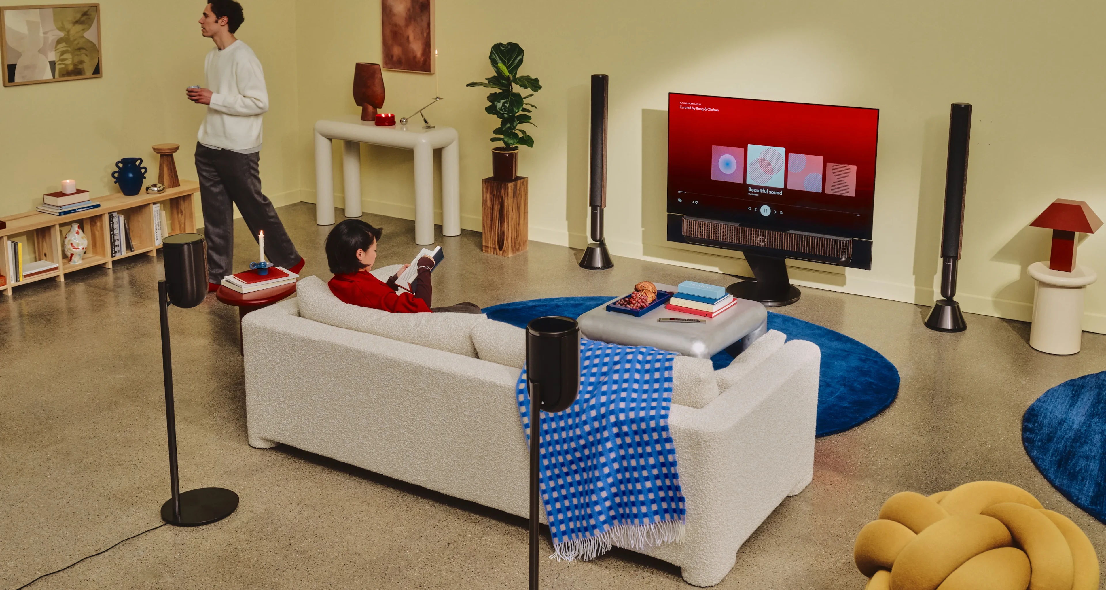Living room scene with a person on couch, watching TV, and another standing.