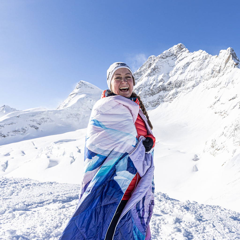 Corinne Weidmann posing with the Lauterbrunnen Valley Original Puffy Blanket against  a snowy mountain background.