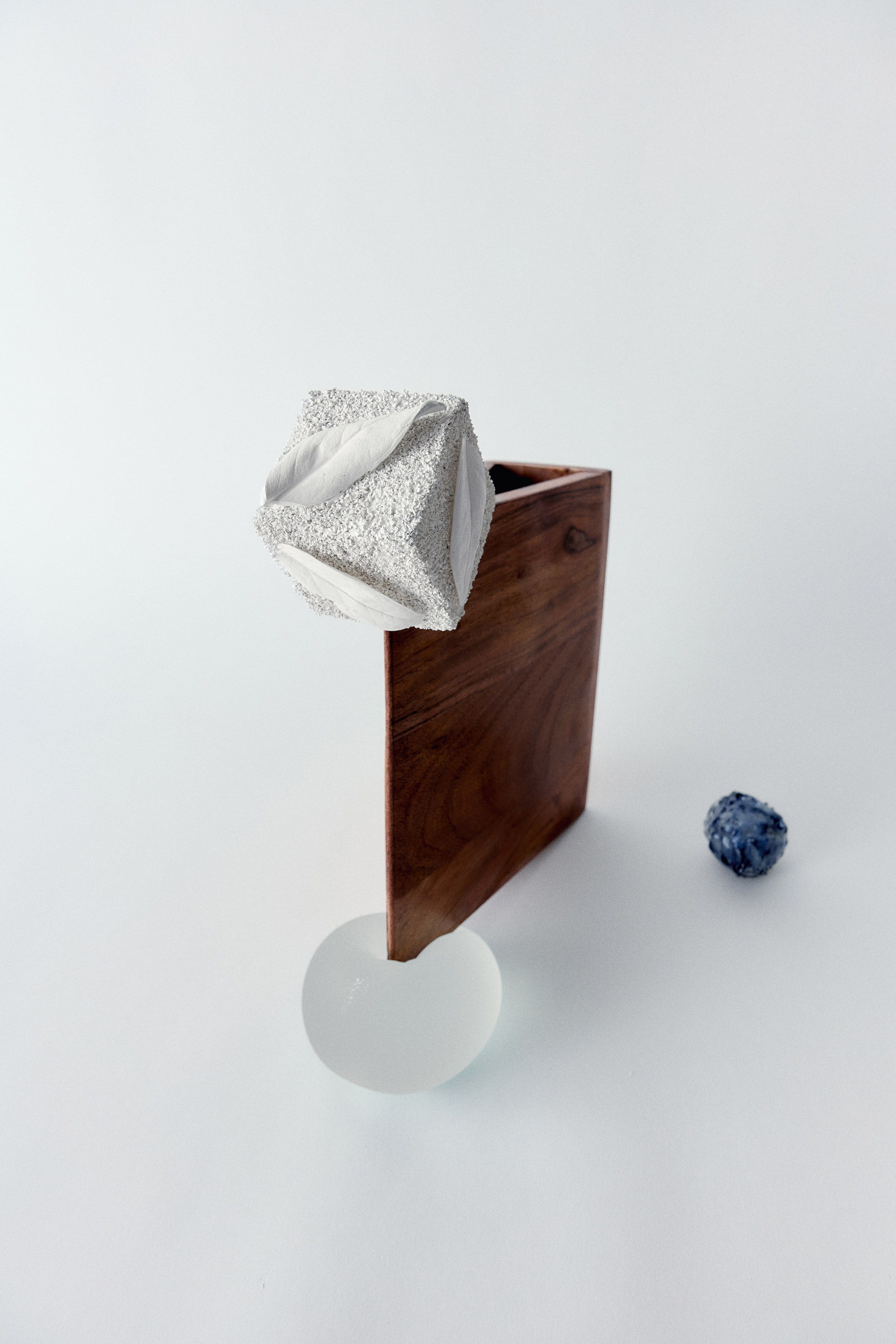 Abstract composition with wooden box, textured object, glass disc, and blue sphere.