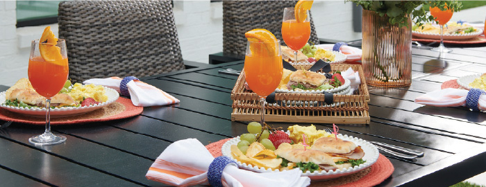 A beautifully set outdoor dining table with colorful drinks and plates of food.