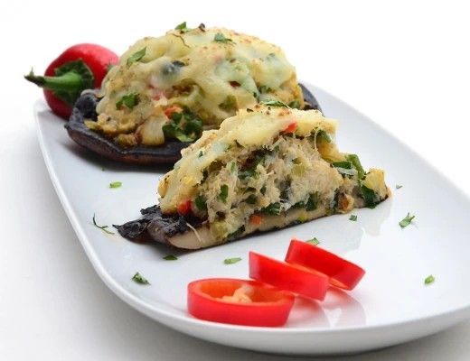 Stuffed mushrooms on a white plate with sliced red peppers.
