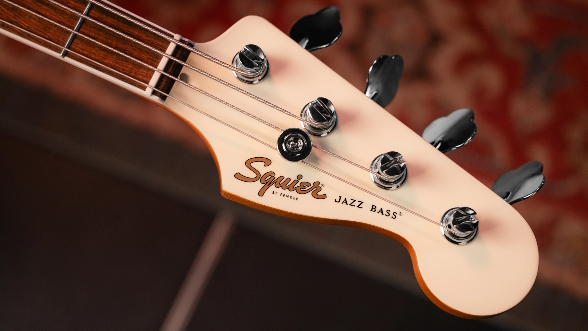 Close-up of a Squier Jazz Bass headstock with tuning pegs and logo.