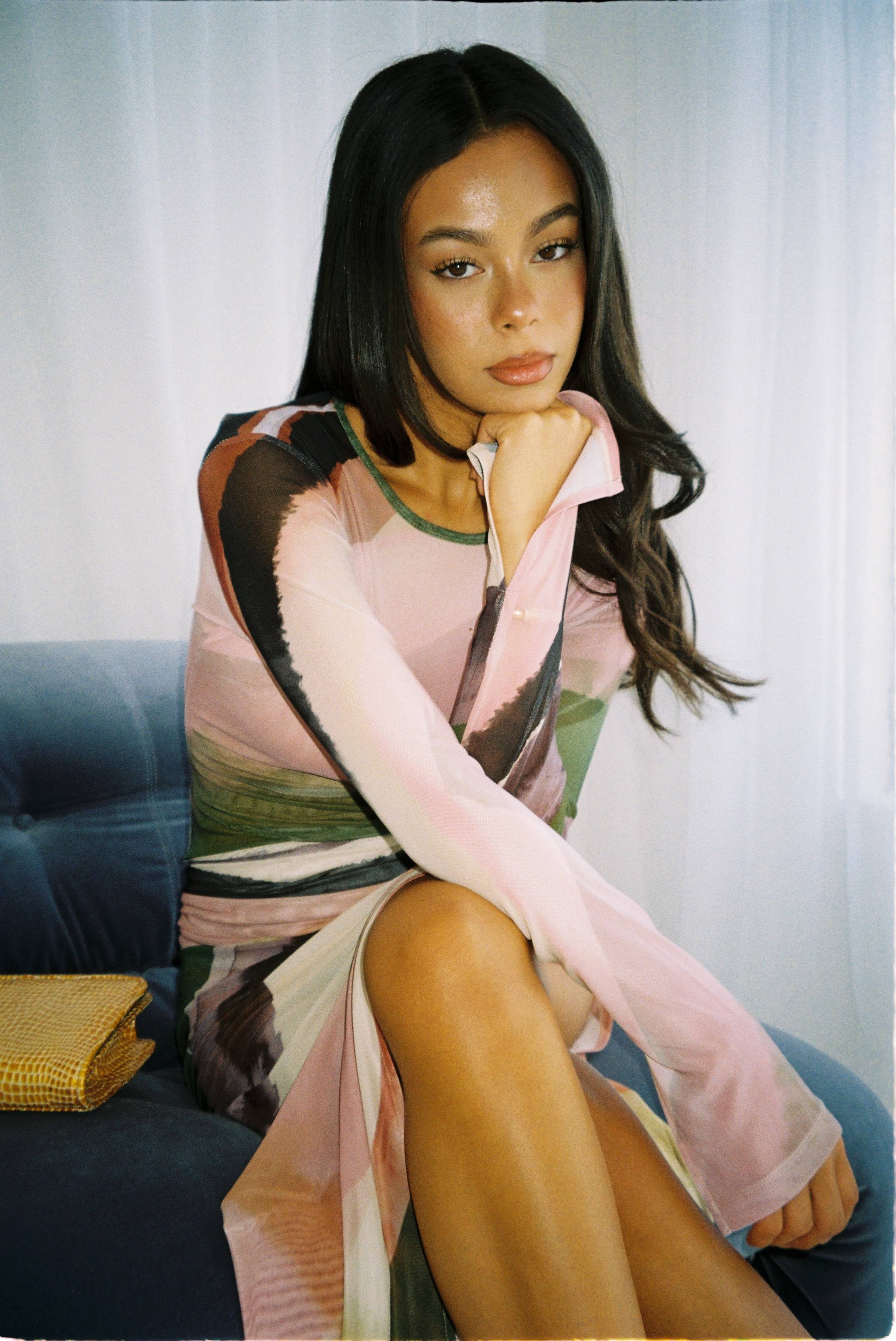 A woman in a colorful dress sitting thoughtfully on a sofa.
