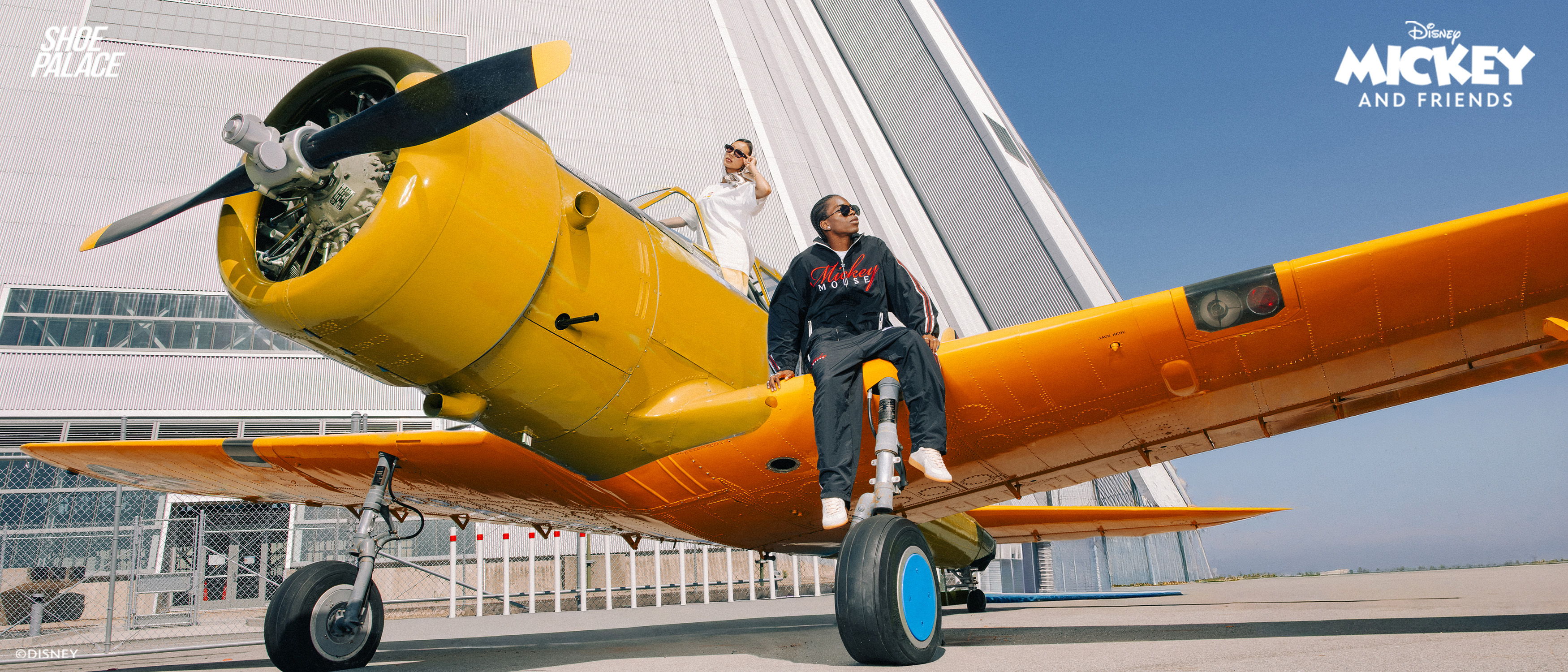 Person sitting on an orange airplane with a propeller, blue sky in background.