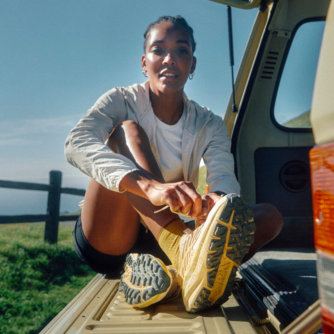 Person sitting on vehicle, wearing yellow shoes, smiling outdoors.