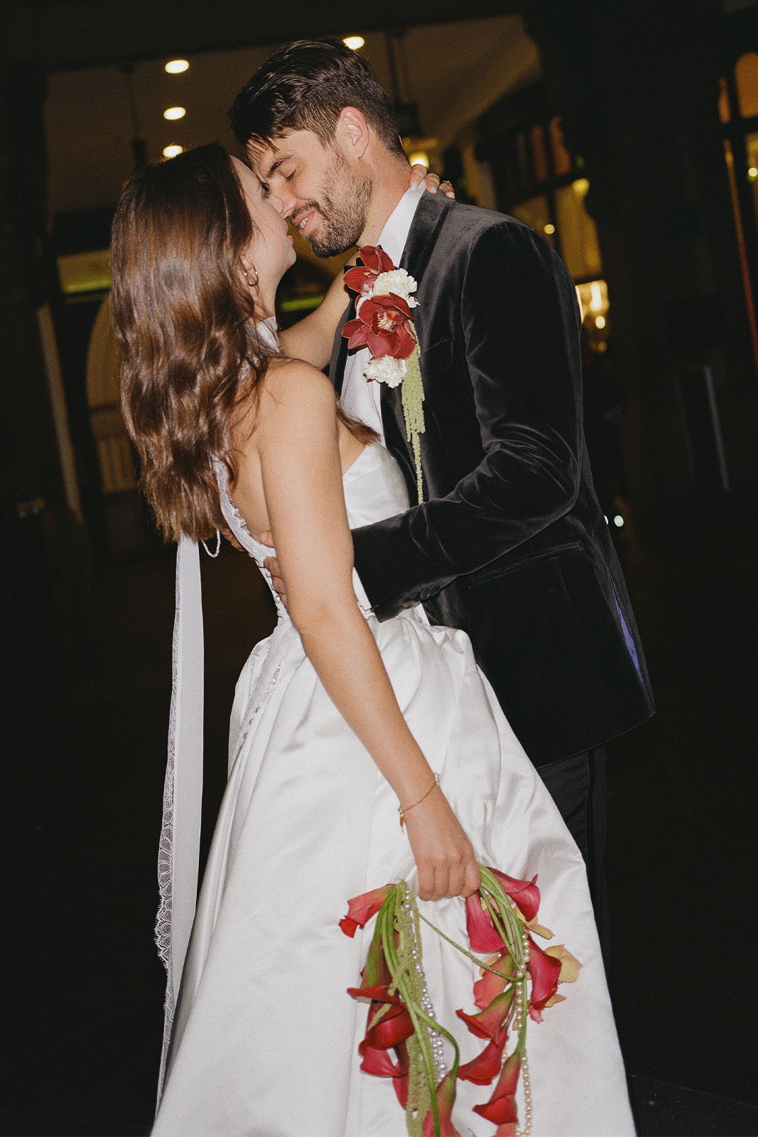 Couple embracing, bride in white dress holding flowers, romantic moment.