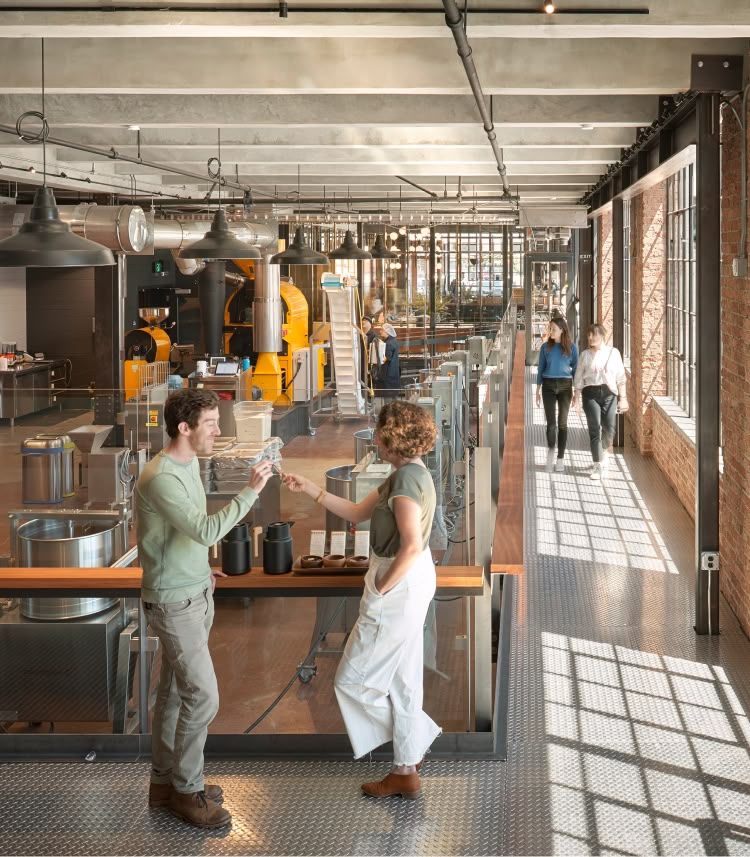 Two people talking in a modern, industrial-style cafe with large windows.