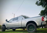 Low-angle rear-quarter view of silver RAM pickup with neon green wheel accents and lifted off-road stance on grass