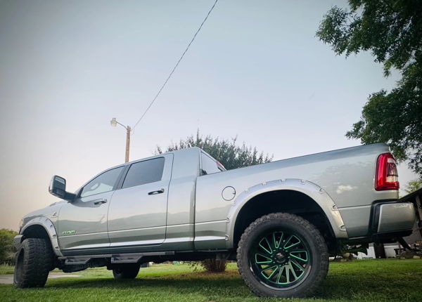 Low-angle rear-quarter view of silver RAM pickup with neon green wheel accents and lifted off-road stance on grass