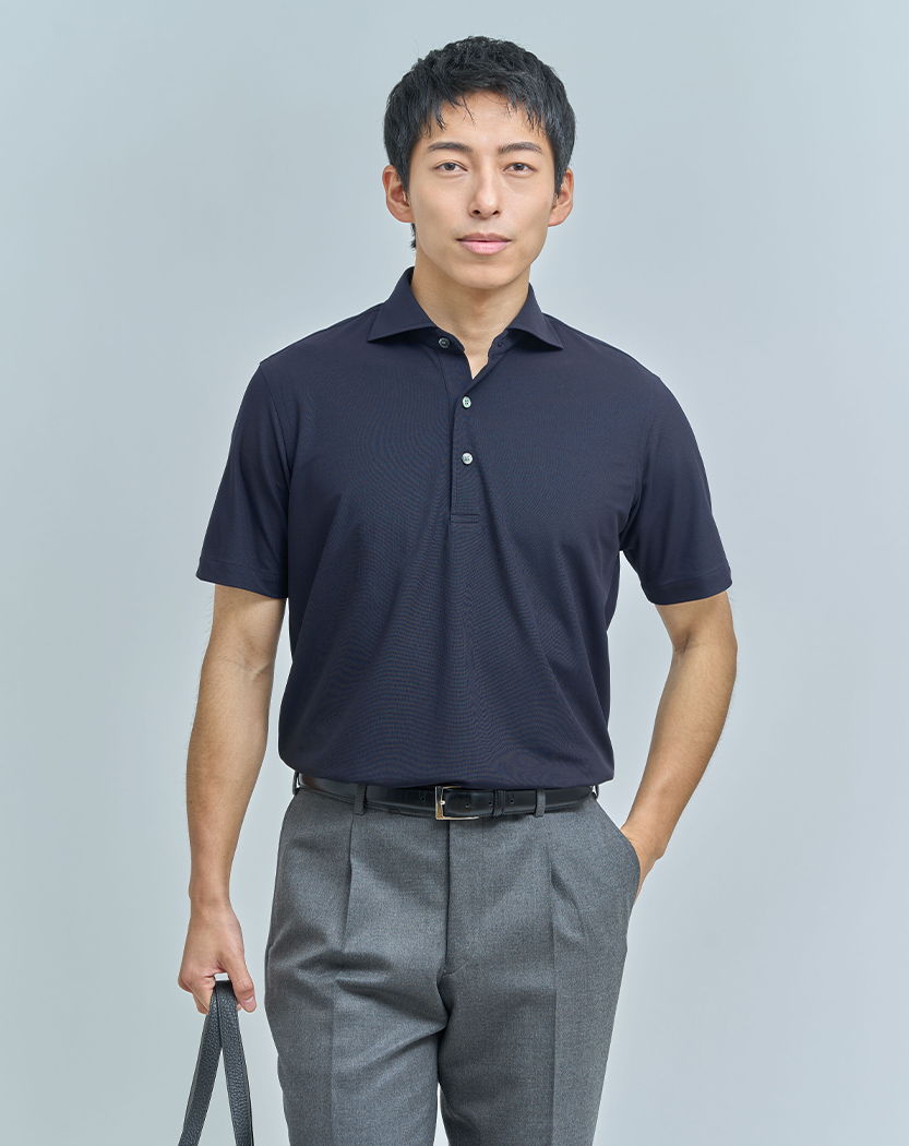 Man in a navy polo shirt and gray trousers, holding a bag.