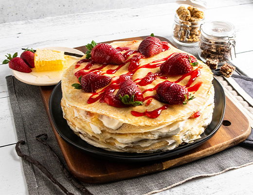 Layered cake topped with strawberries and sauce, served on a wooden platter.