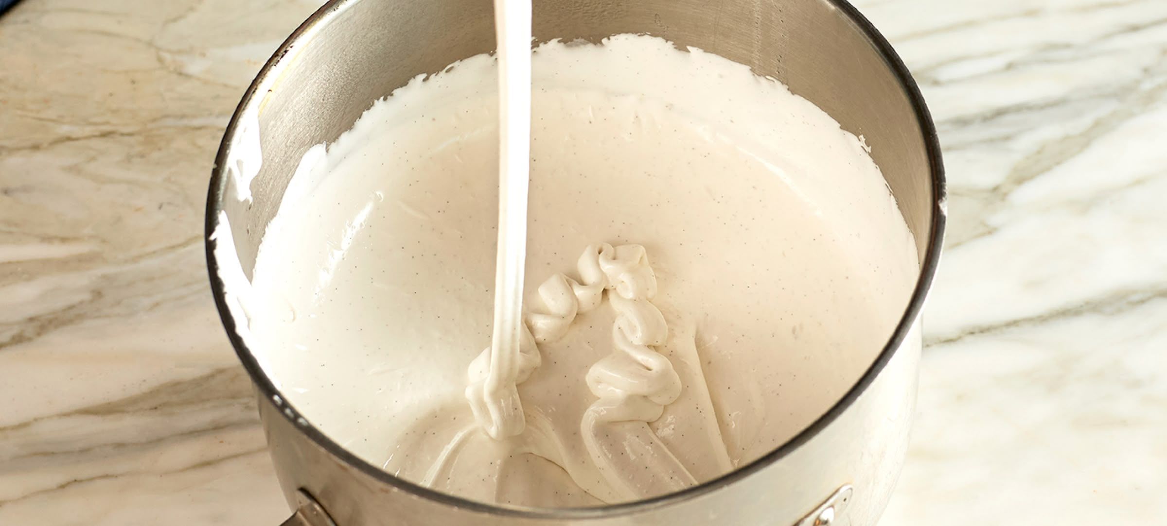 A metal bowl filled with creamy liquid being poured.
