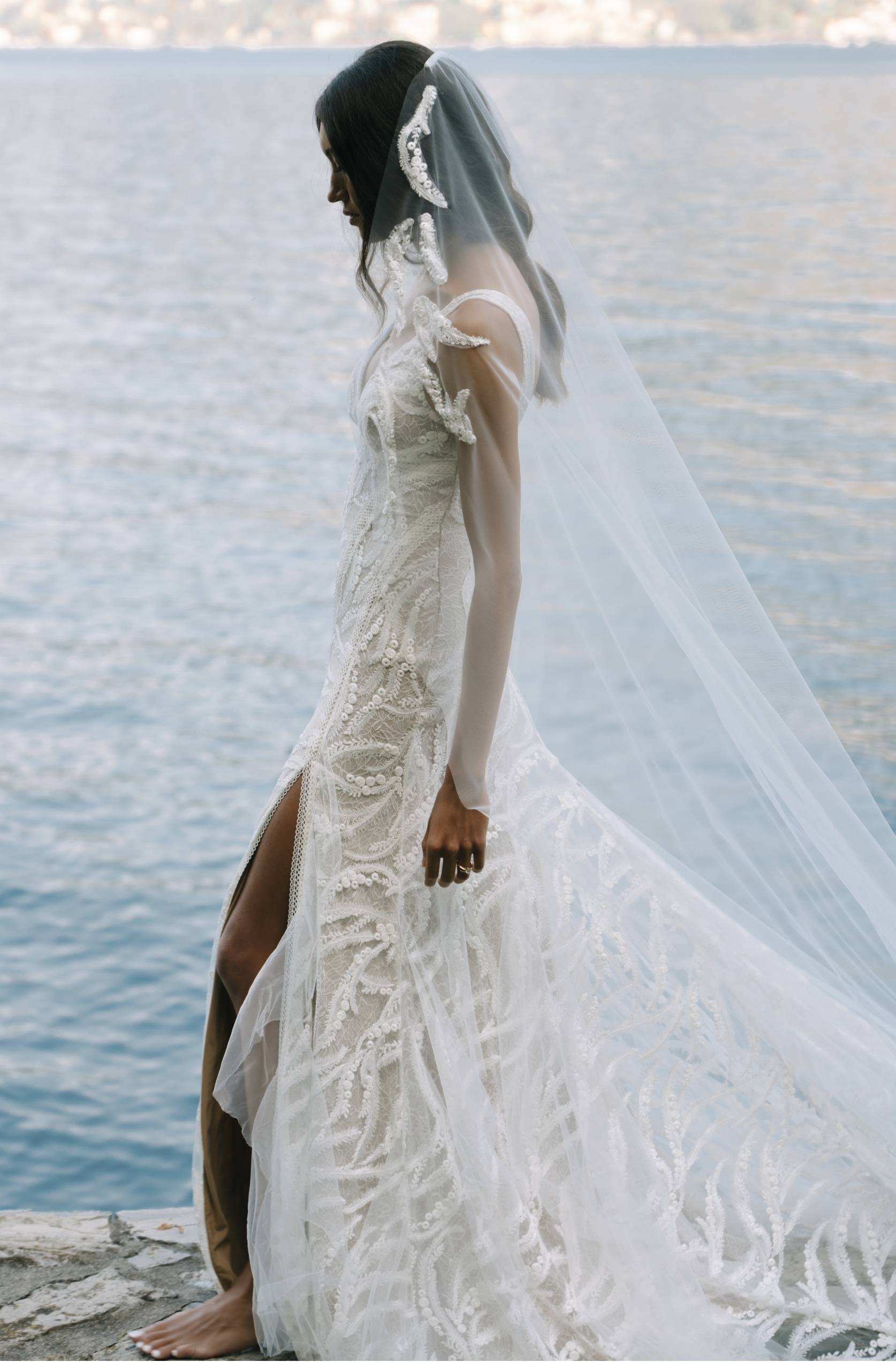 Model in Grace Loves Lace Solstice Gown and Solstice Veil with Italian coastline in background
