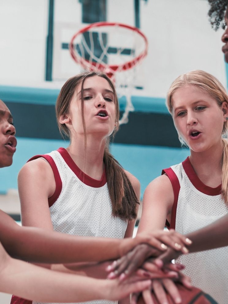 school girls basketball team in huddle on the court wearing white and maroon uniforms
