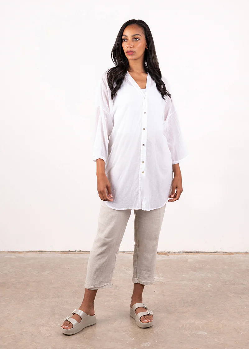 A model wearing a semi sheer white oversized button down shirt with off white linen trousers and chunky platform slides, 