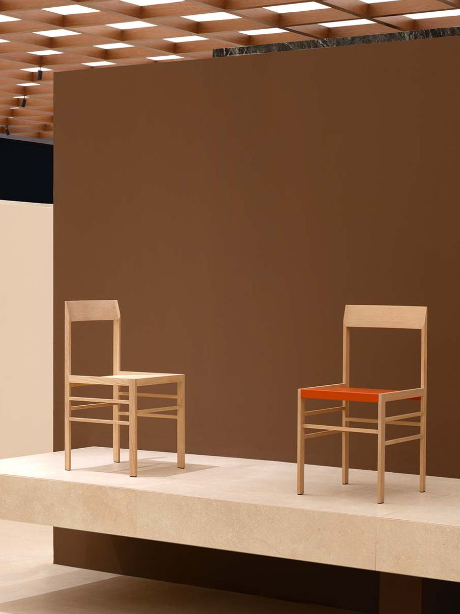Two wooden METRIC chairs on a display against a brown wall.
