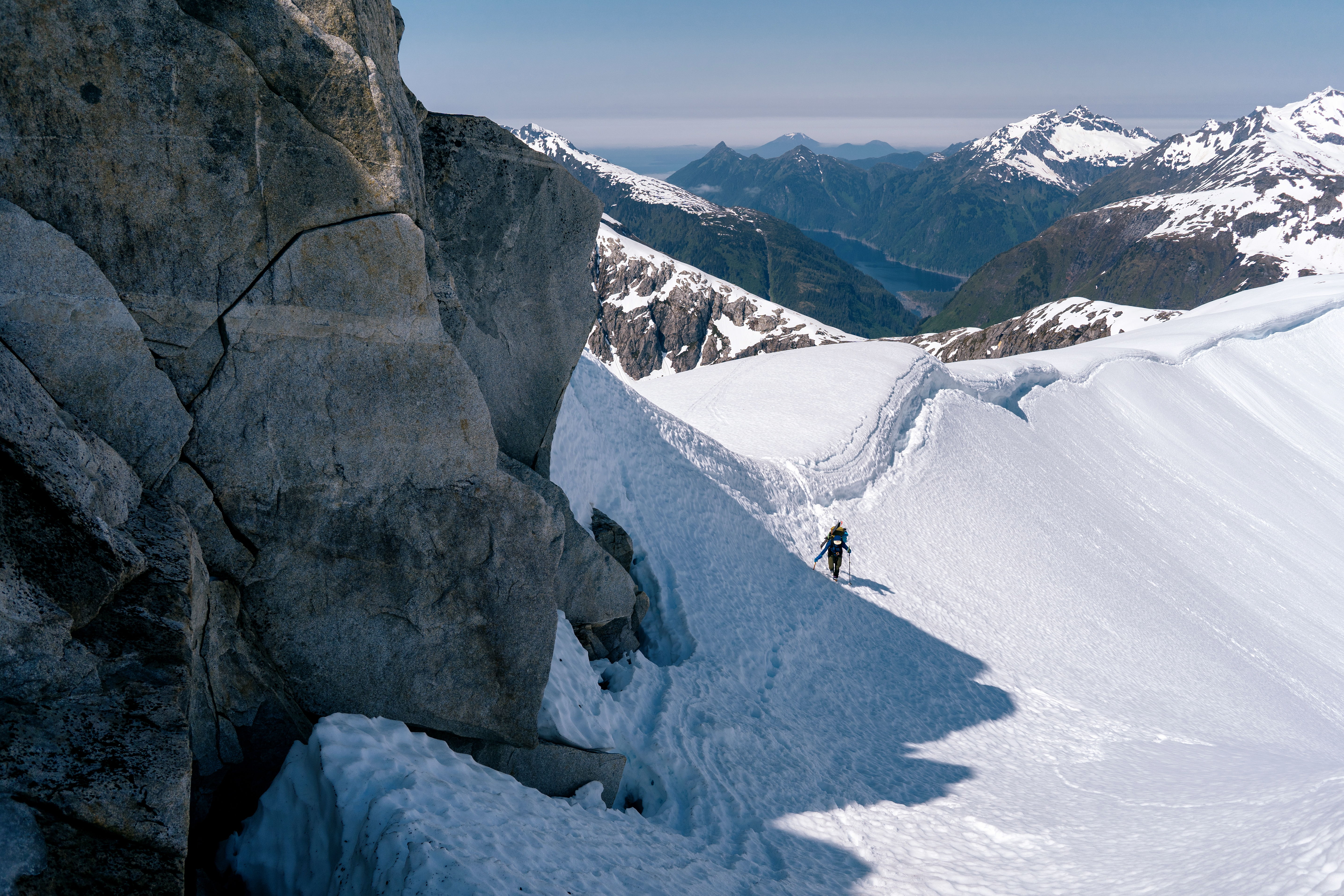 A splitboarder traversing a snowy mountain landscape with rocky formations.
