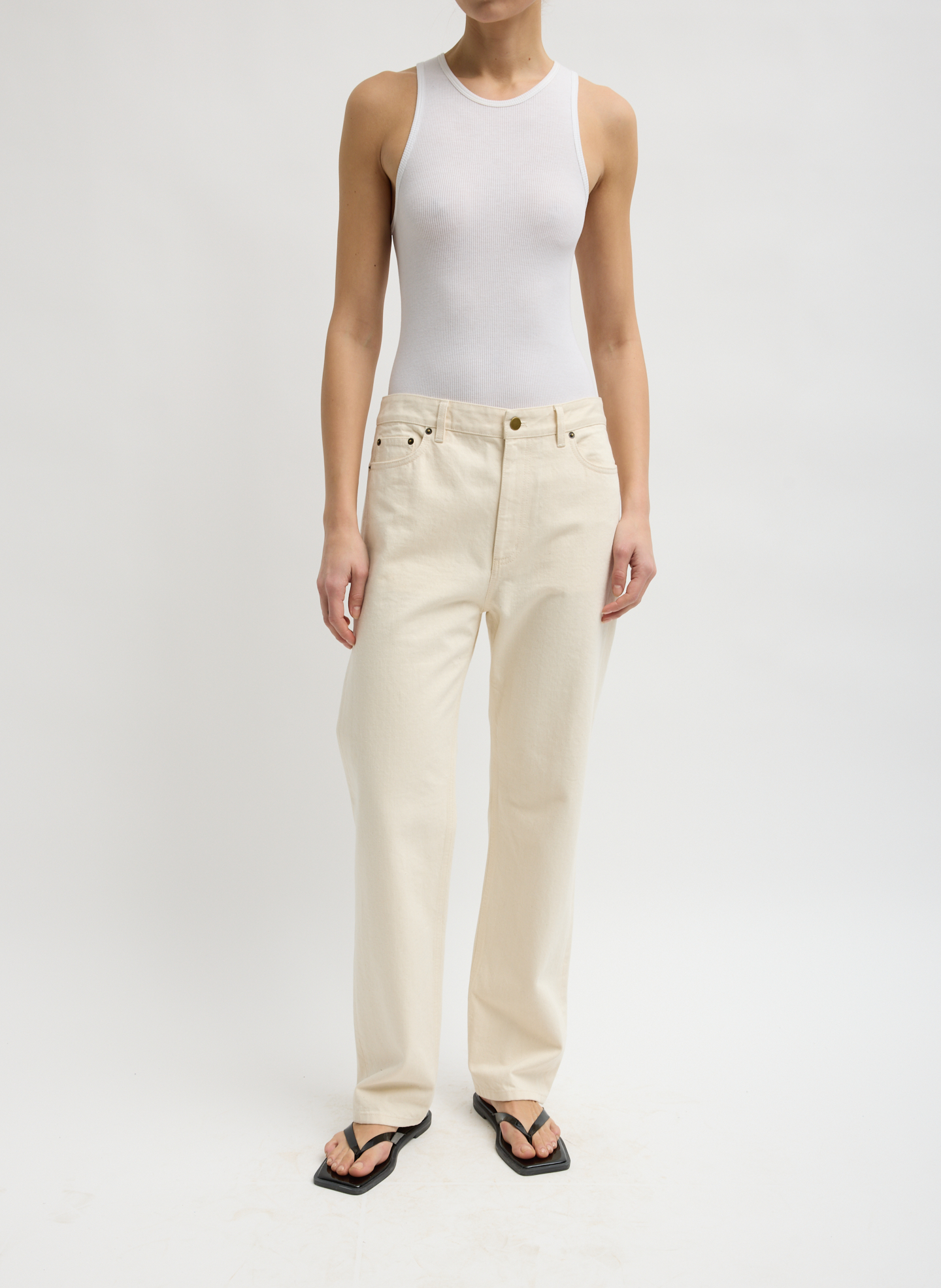 A person wearing a white tank top and beige pants, standing.