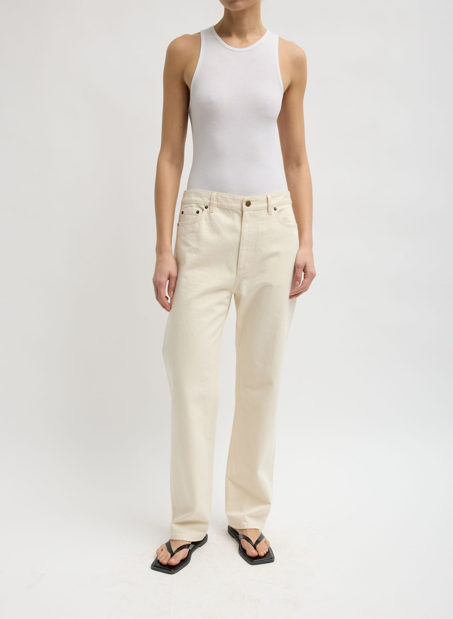 A person wearing a white tank top and beige pants, standing.